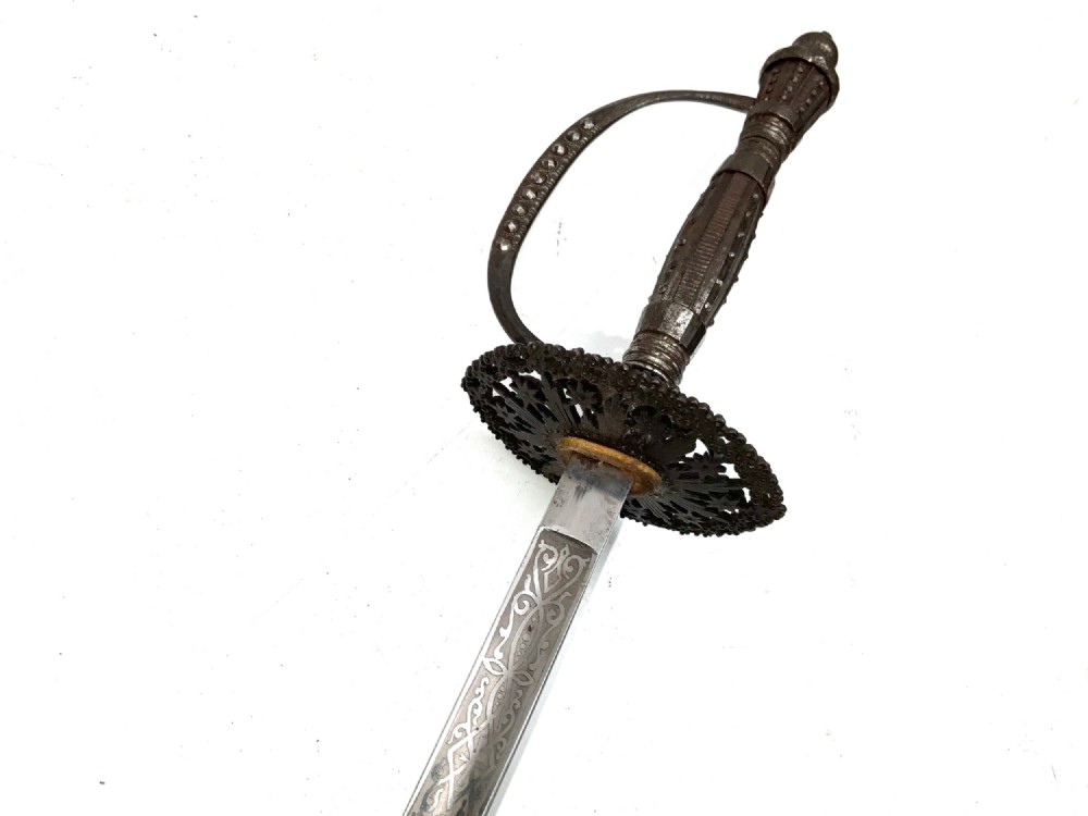 An 18th-century rapier sword featuring a dark leather scabbard and an intricately pierced round steel hilt guard. View VI