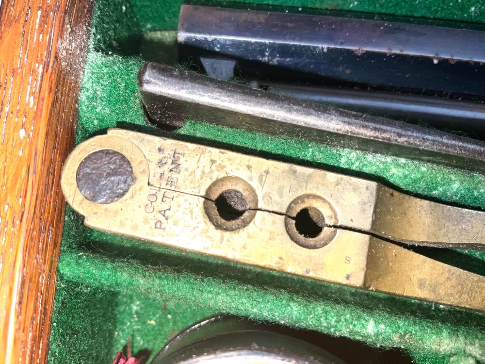 An open fitted wooden presentation case containing a .31 calibre percussion revolver, a brass powder flask, a bullet mould, and an instruction label attached to the inner lid. View VI