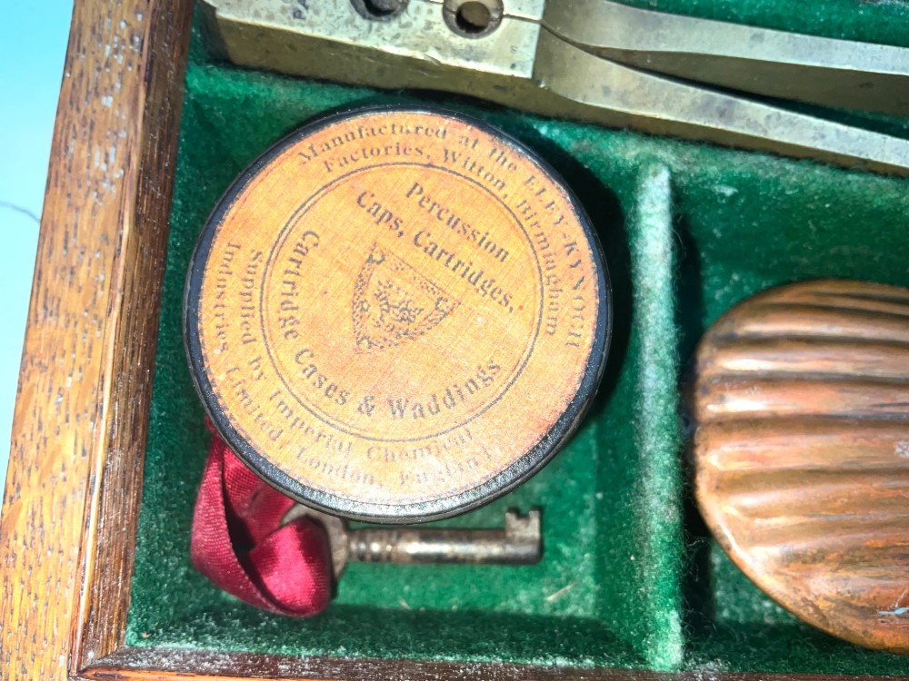 An open fitted wooden presentation case containing a .31 calibre percussion revolver, a brass powder flask, a bullet mould, and an instruction label attached to the inner lid. View VII
