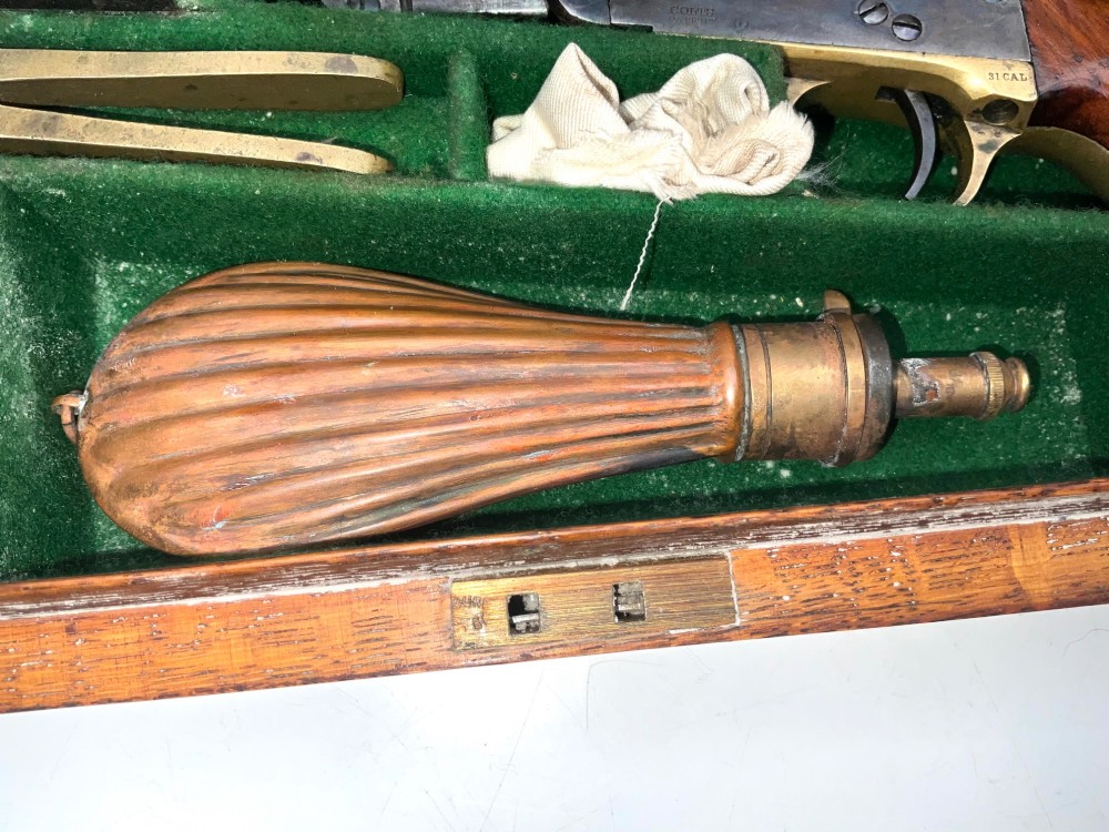 An open fitted wooden presentation case containing a .31 calibre percussion revolver, a brass powder flask, a bullet mould, and an instruction label attached to the inner lid. View VIII
