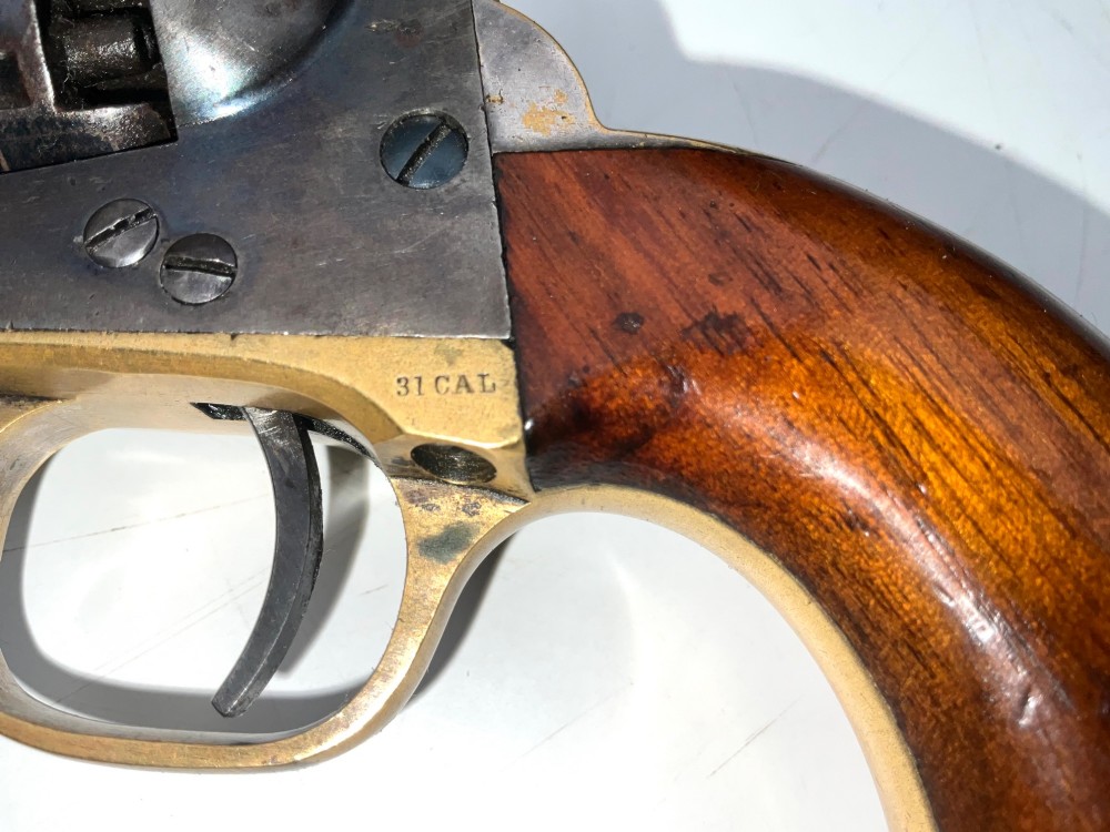 An open fitted wooden presentation case containing a .31 calibre percussion revolver, a brass powder flask, a bullet mould, and an instruction label attached to the inner lid. View IX