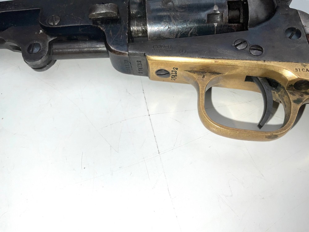 An open fitted wooden presentation case containing a .31 calibre percussion revolver, a brass powder flask, a bullet mould, and an instruction label attached to the inner lid. View X