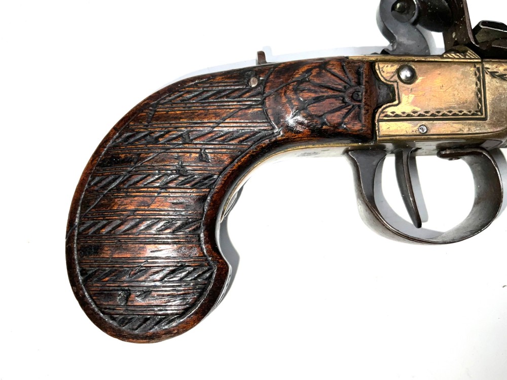 An antique Georgian flintlock overcoat pistol featuring a turned brass cannon barrel, engraved boxlock mechanism, and carved wooden handle. View II