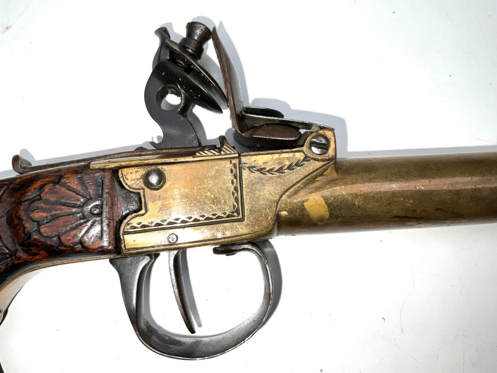 An antique Georgian flintlock overcoat pistol featuring a turned brass cannon barrel, engraved boxlock mechanism, and carved wooden handle. View III