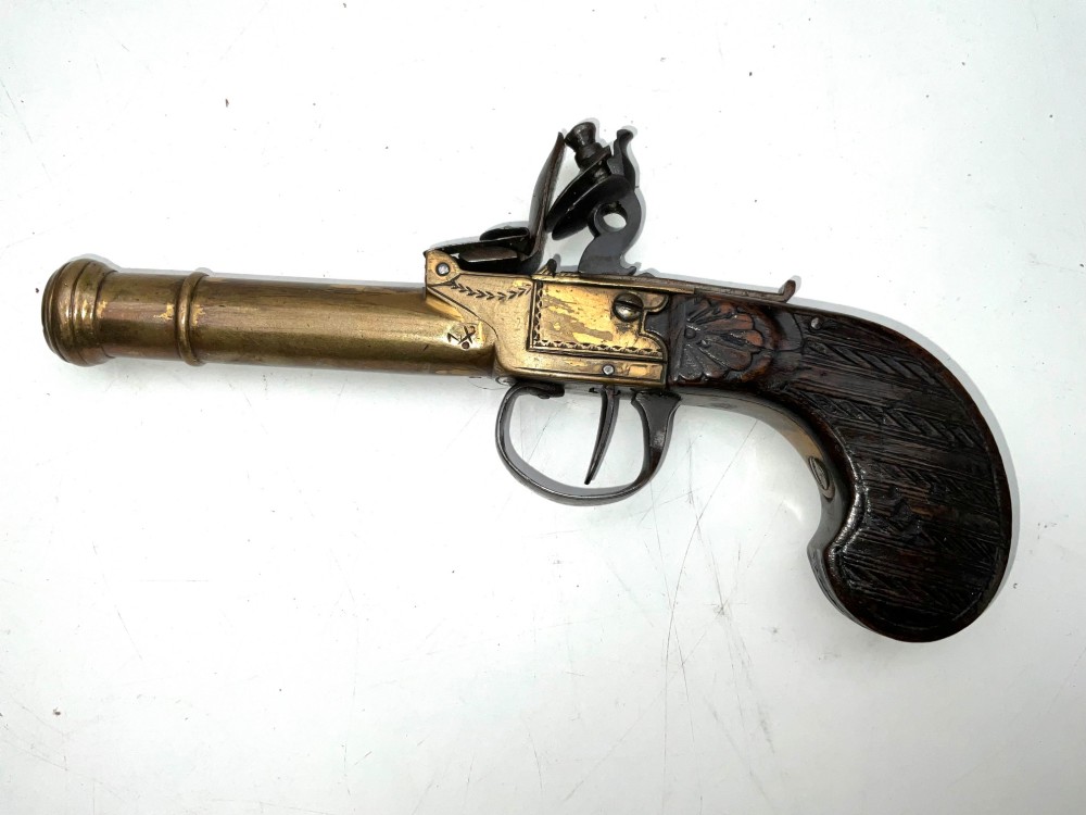 An antique Georgian flintlock overcoat pistol featuring a turned brass cannon barrel, engraved boxlock mechanism, and carved wooden handle. View V