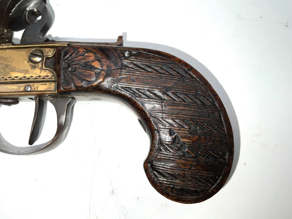 An antique Georgian flintlock overcoat pistol featuring a turned brass cannon barrel, engraved boxlock mechanism, and carved wooden handle. View VI