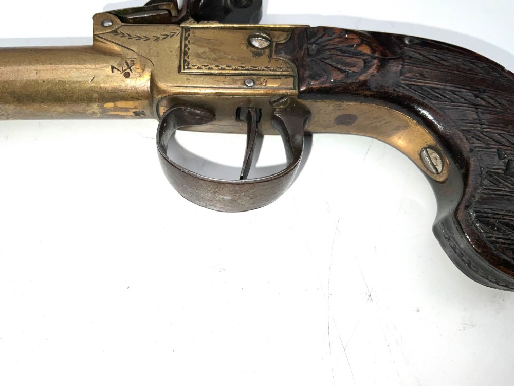 An antique Georgian flintlock overcoat pistol featuring a turned brass cannon barrel, engraved boxlock mechanism, and carved wooden handle. View VII