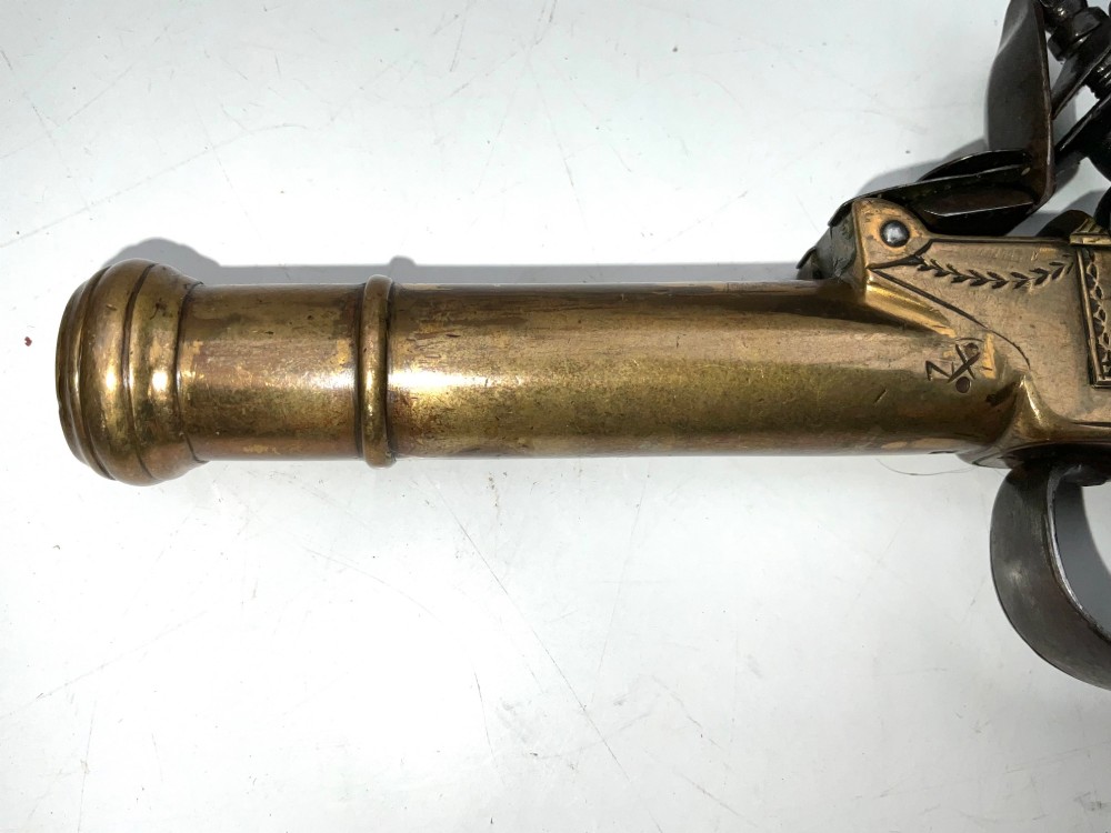 An antique Georgian flintlock overcoat pistol featuring a turned brass cannon barrel, engraved boxlock mechanism, and carved wooden handle. View VIII