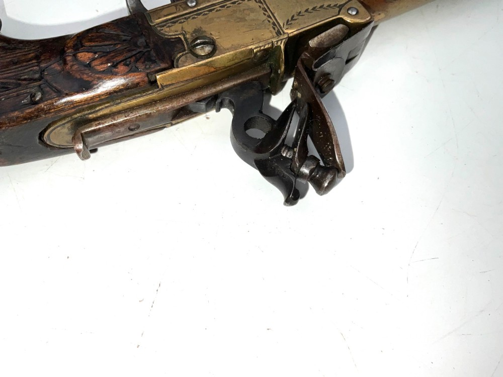 An antique Georgian flintlock overcoat pistol featuring a turned brass cannon barrel, engraved boxlock mechanism, and carved wooden handle. View IX
