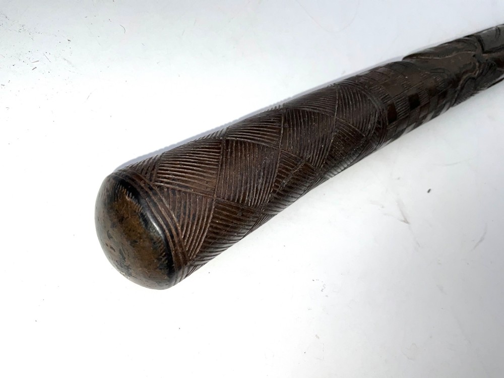 A tapered dark brown carved wooden Japanese bokken training stick featuring surface relief carvings. View II