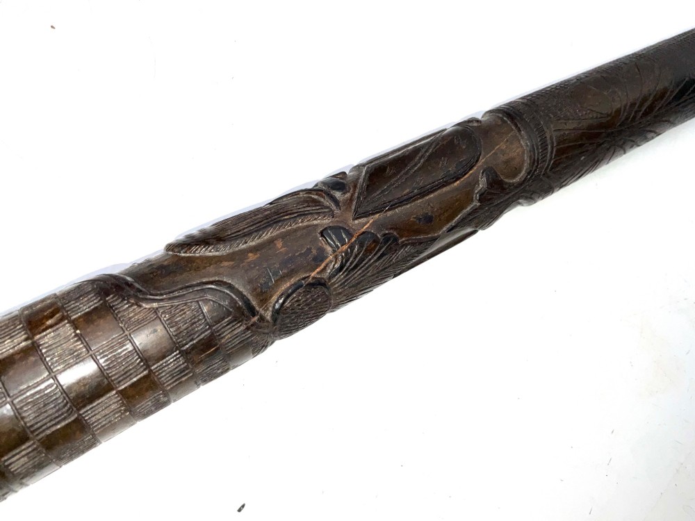 A tapered dark brown carved wooden Japanese bokken training stick featuring surface relief carvings. View III