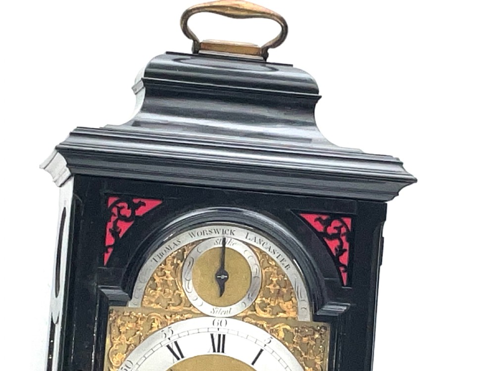 An eighteenth-century ebonised Georgian bracket clock featuring a brass carrying handle, an arched glass front door, and a brass dial with silvered chapter ring. View IV