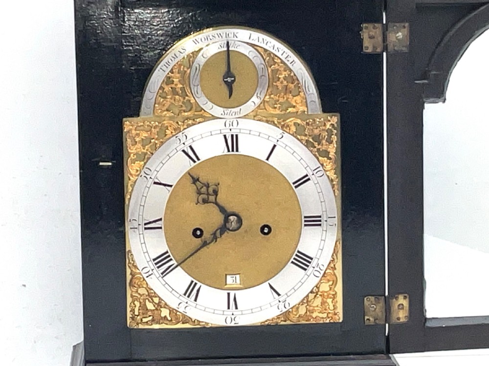 An eighteenth-century ebonised Georgian bracket clock featuring a brass carrying handle, an arched glass front door, and a brass dial with silvered chapter ring. View V