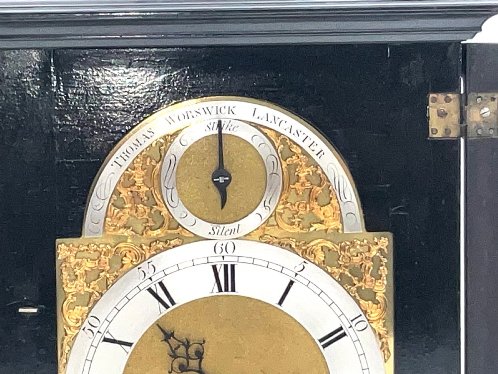 An eighteenth-century ebonised Georgian bracket clock featuring a brass carrying handle, an arched glass front door, and a brass dial with silvered chapter ring. View VI