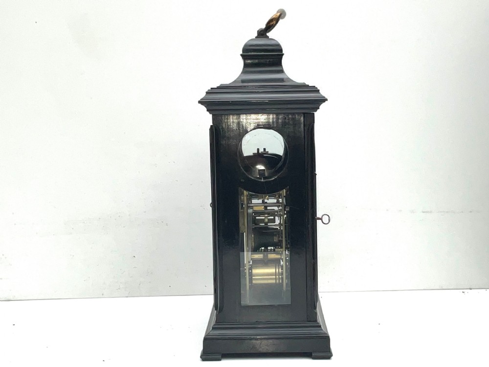 An eighteenth-century ebonised Georgian bracket clock featuring a brass carrying handle, an arched glass front door, and a brass dial with silvered chapter ring. View VII