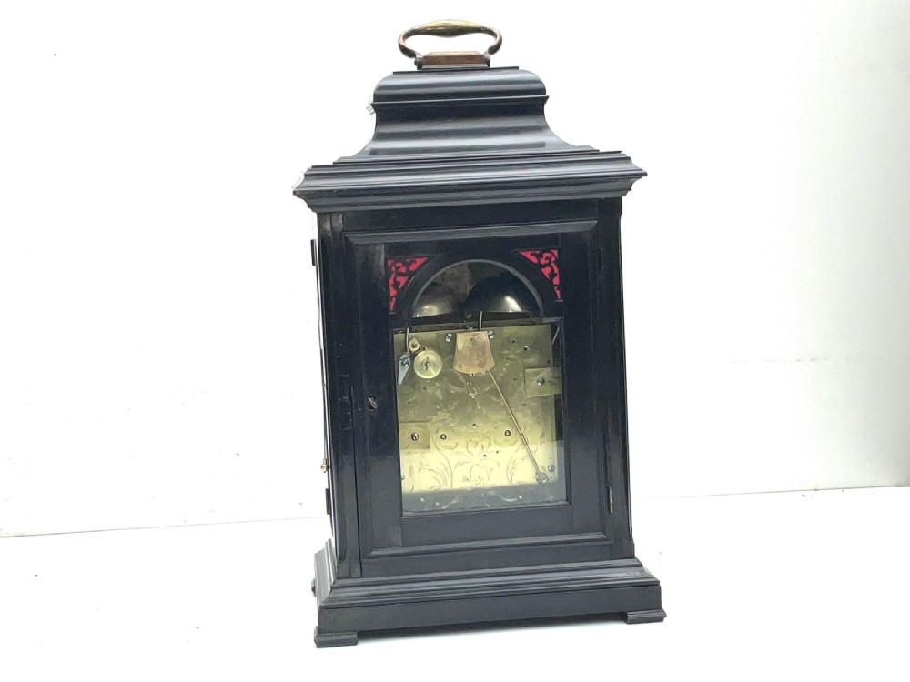 An eighteenth-century ebonised Georgian bracket clock featuring a brass carrying handle, an arched glass front door, and a brass dial with silvered chapter ring. View VIII