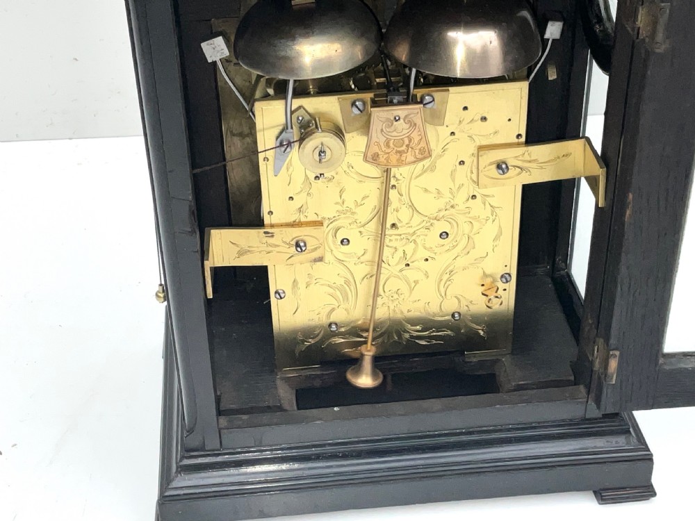 An eighteenth-century ebonised Georgian bracket clock featuring a brass carrying handle, an arched glass front door, and a brass dial with silvered chapter ring. View IX