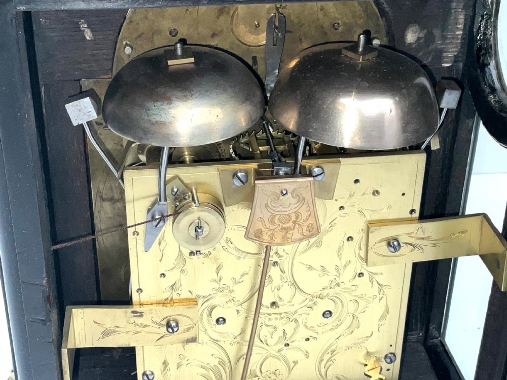 An eighteenth-century ebonised Georgian bracket clock featuring a brass carrying handle, an arched glass front door, and a brass dial with silvered chapter ring. View X