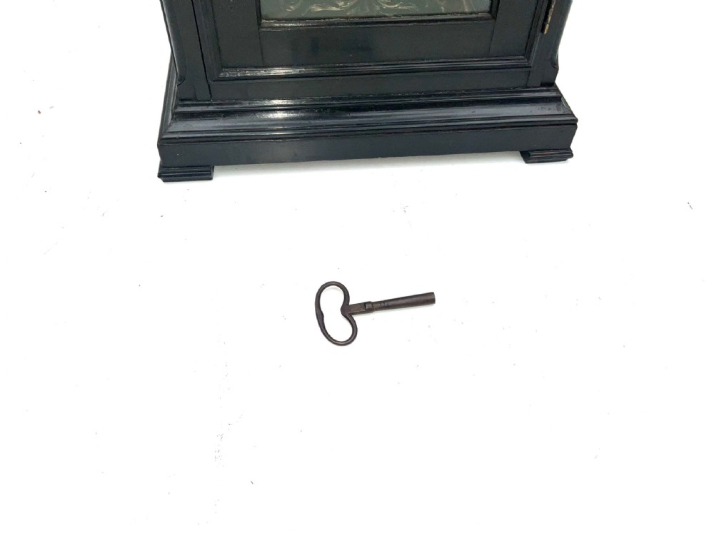 An eighteenth-century ebonised Georgian bracket clock featuring a brass carrying handle, an arched glass front door, and a brass dial with silvered chapter ring. View XII