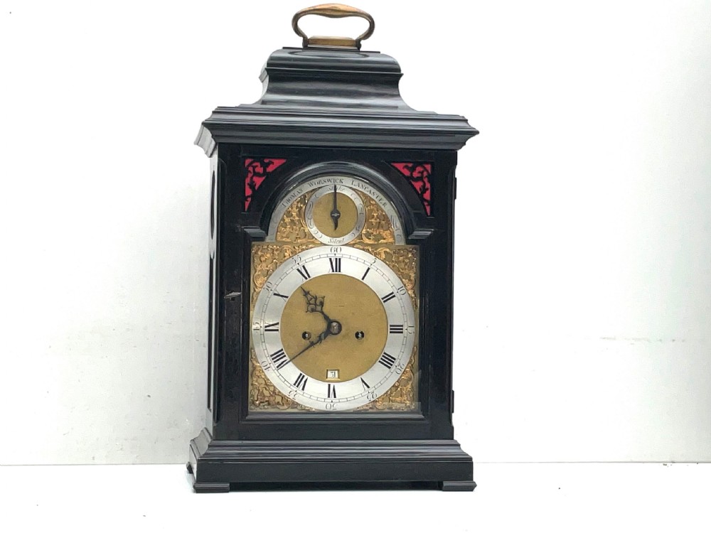 An eighteenth-century ebonised Georgian bracket clock featuring a brass carrying handle, an arched glass front door, and a brass dial with silvered chapter ring. View XIII