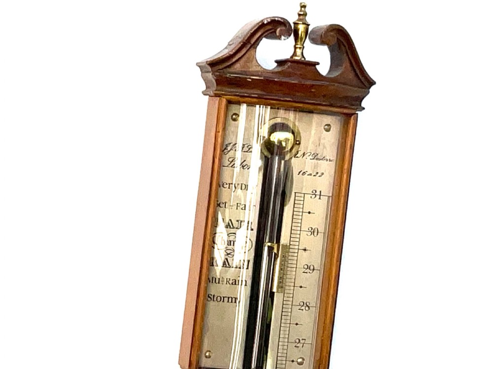 A wall-mounted antique Georgian stick barometer crafted from figured satinwood, featuring a brass finial, pediment top, and glass-fronted silvered scale. View X