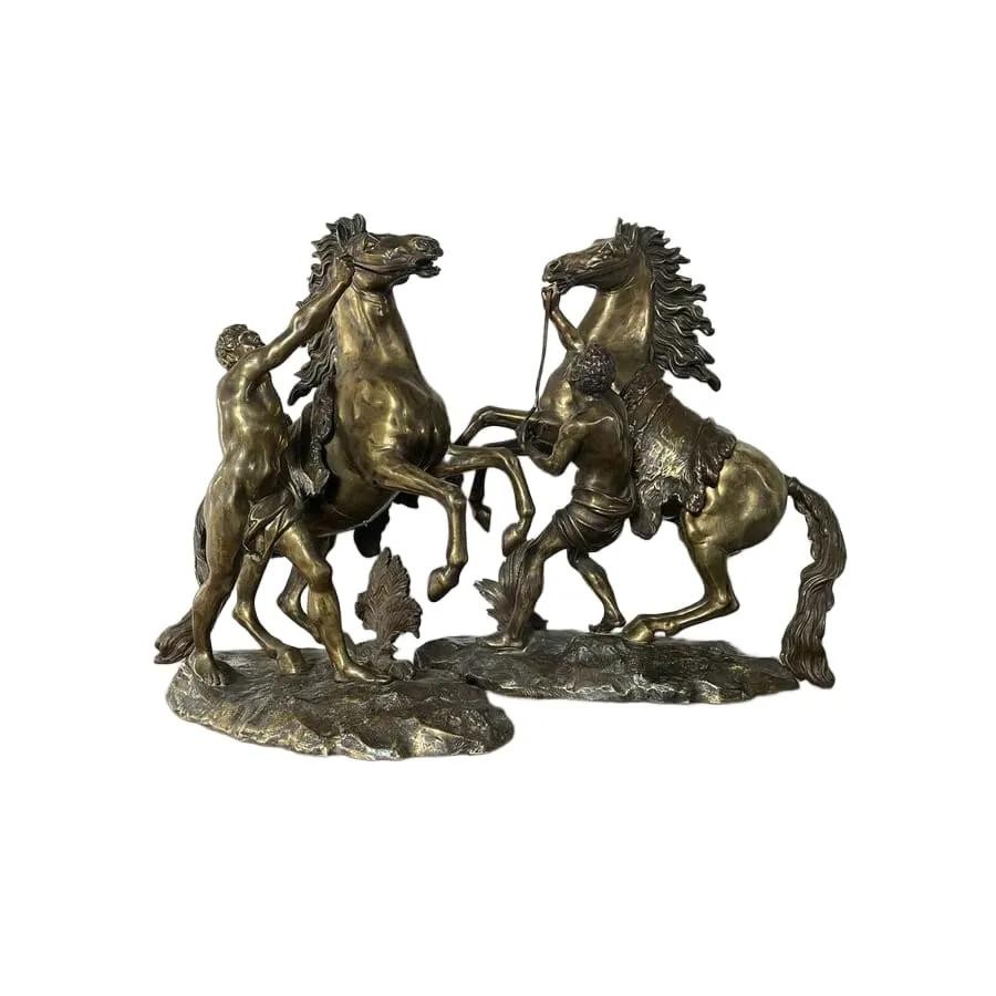 A pair of detailed gilt-bronze sculptures depicting rearing horses held by classical male handlers on naturalistic bases.