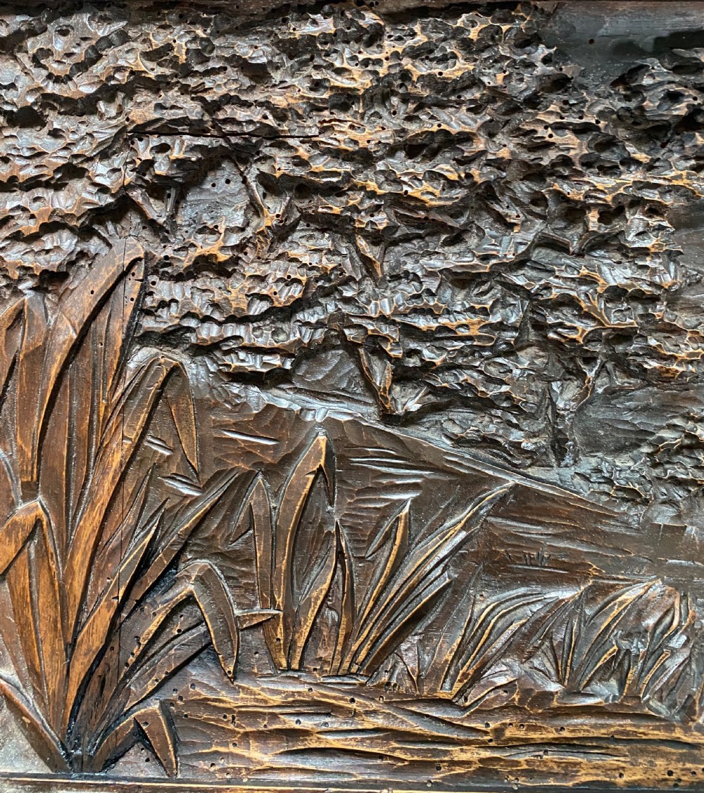 A horizontal dark walnut wood panel with a relief carving of a hunting dog in a landscape, surrounded by a carved decorative border. View II