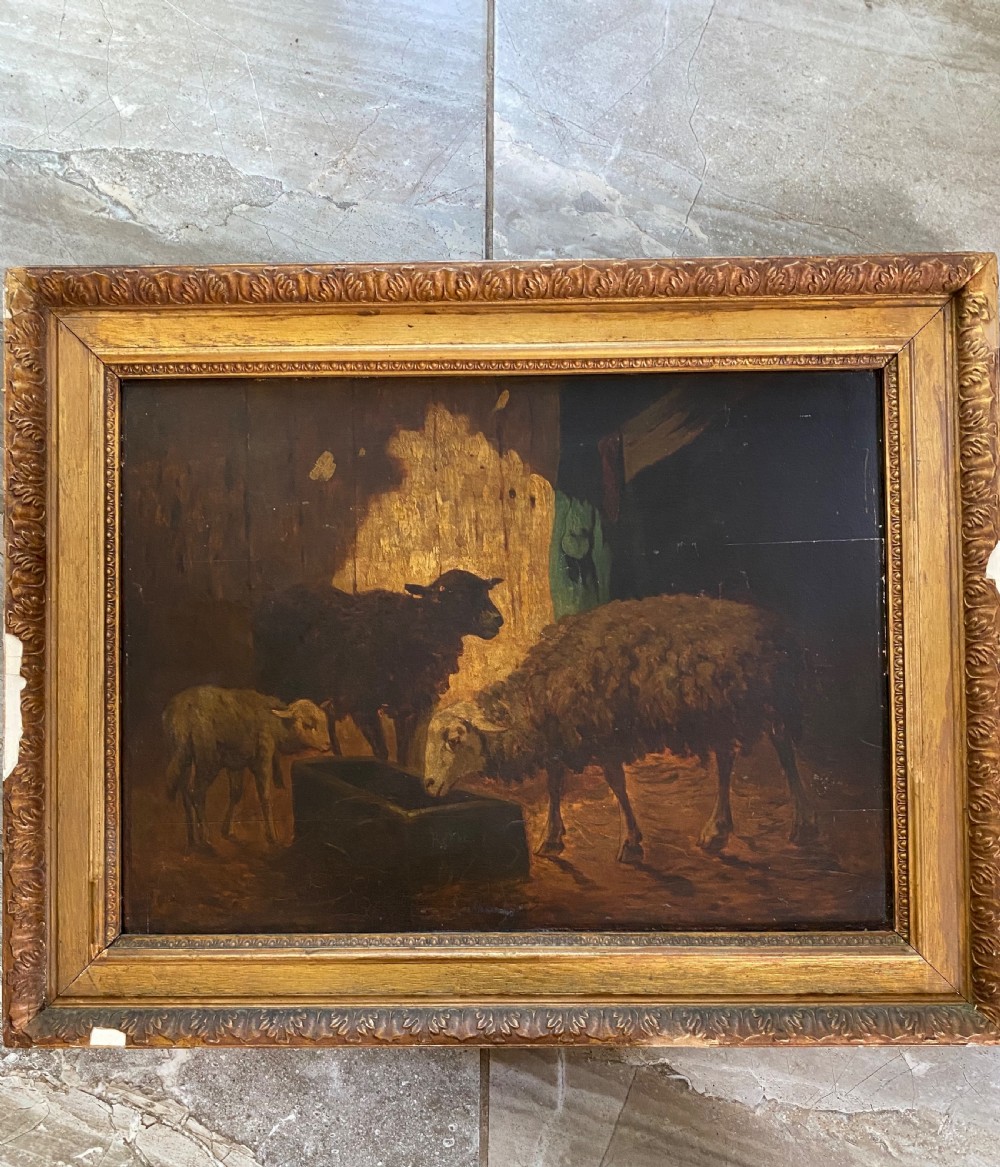 An antique oil painting depicting sheep and a lamb feeding at a trough inside a barn, housed in an ornate gilded frame.