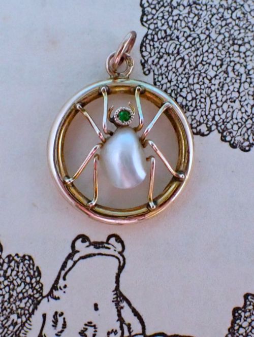 fig 2. A circular 9ct gold pendant framing a central spider motif set with a pearl abdomen and a small round emerald head.