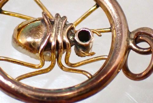 fig 3. A circular 9ct gold pendant framing a central spider motif set with a pearl abdomen and a small round emerald head.