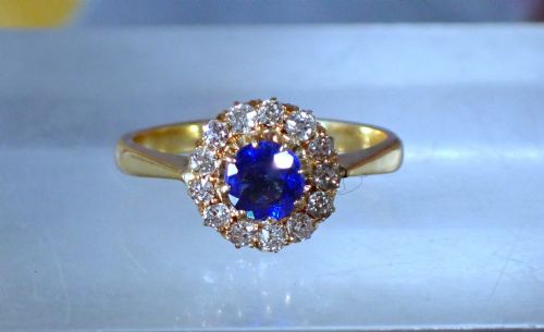 fig 1. An Edwardian 18ct yellow gold ring featuring a central round blue sapphire surrounded by a floral halo of small diamonds.