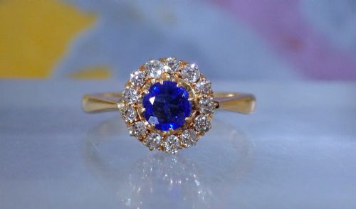 fig 3. An Edwardian 18ct yellow gold ring featuring a central round blue sapphire surrounded by a floral halo of small diamonds.