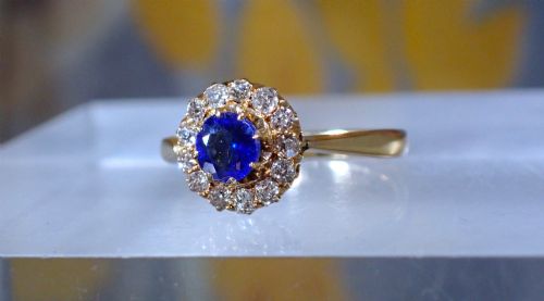 fig 4. An Edwardian 18ct yellow gold ring featuring a central round blue sapphire surrounded by a floral halo of small diamonds.
