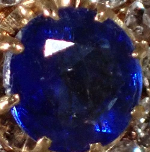 An Edwardian 18ct yellow gold ring featuring a central round blue sapphire surrounded by a floral halo of small diamonds. View VII