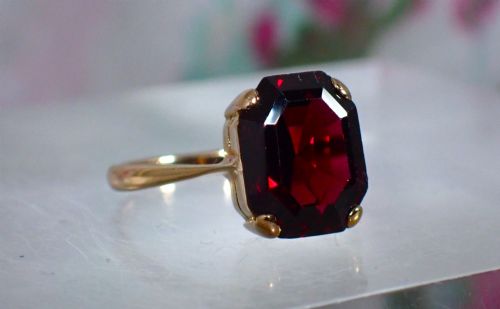 fig 1. An Art Deco style 9ct yellow gold ring featuring a large, rectangular emerald-cut deep red garnet held by four corner prongs on a slender gold band.