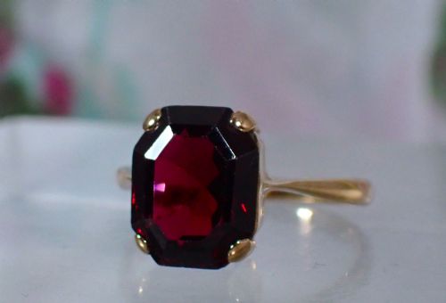 fig 2. An Art Deco style 9ct yellow gold ring featuring a large, rectangular emerald-cut deep red garnet held by four corner prongs on a slender gold band.