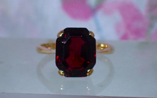fig 3. An Art Deco style 9ct yellow gold ring featuring a large, rectangular emerald-cut deep red garnet held by four corner prongs on a slender gold band.
