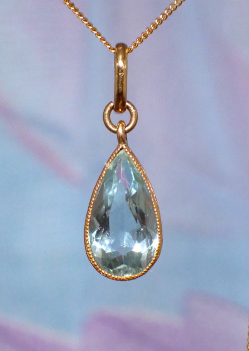 fig 1. A pear-shaped pale blue aquamarine gemstone set in a yellow gold bezel pendant suspended from a fine gold chain.