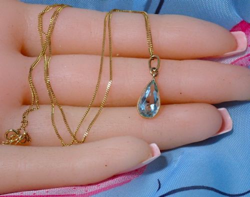 fig 2. A pear-shaped pale blue aquamarine gemstone set in a yellow gold bezel pendant suspended from a fine gold chain.