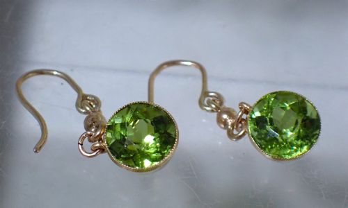 fig 1. Pair of antique Edwardian 15ct gold drop earrings featuring circular faceted green peridots in collet settings suspended from wire hooks.