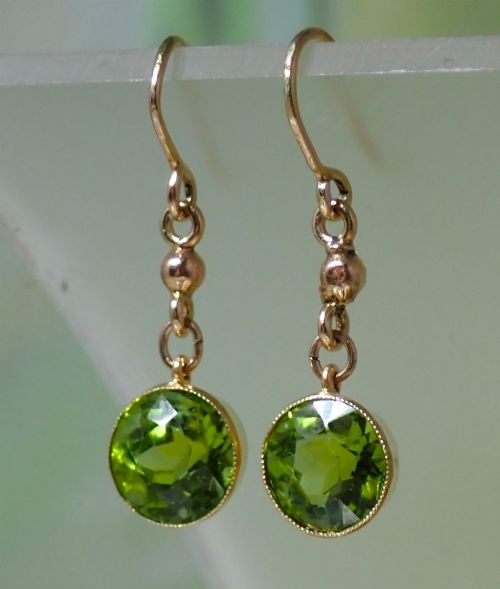 fig 2. Pair of antique Edwardian 15ct gold drop earrings featuring circular faceted green peridots in collet settings suspended from wire hooks.