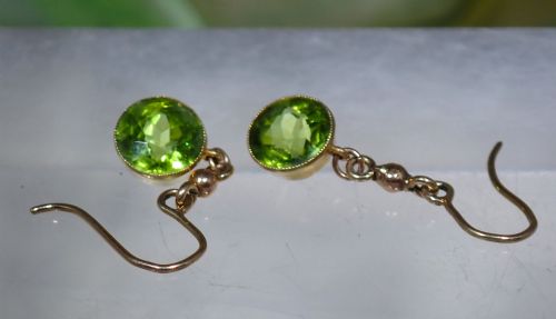fig 3. Pair of antique Edwardian 15ct gold drop earrings featuring circular faceted green peridots in collet settings suspended from wire hooks.