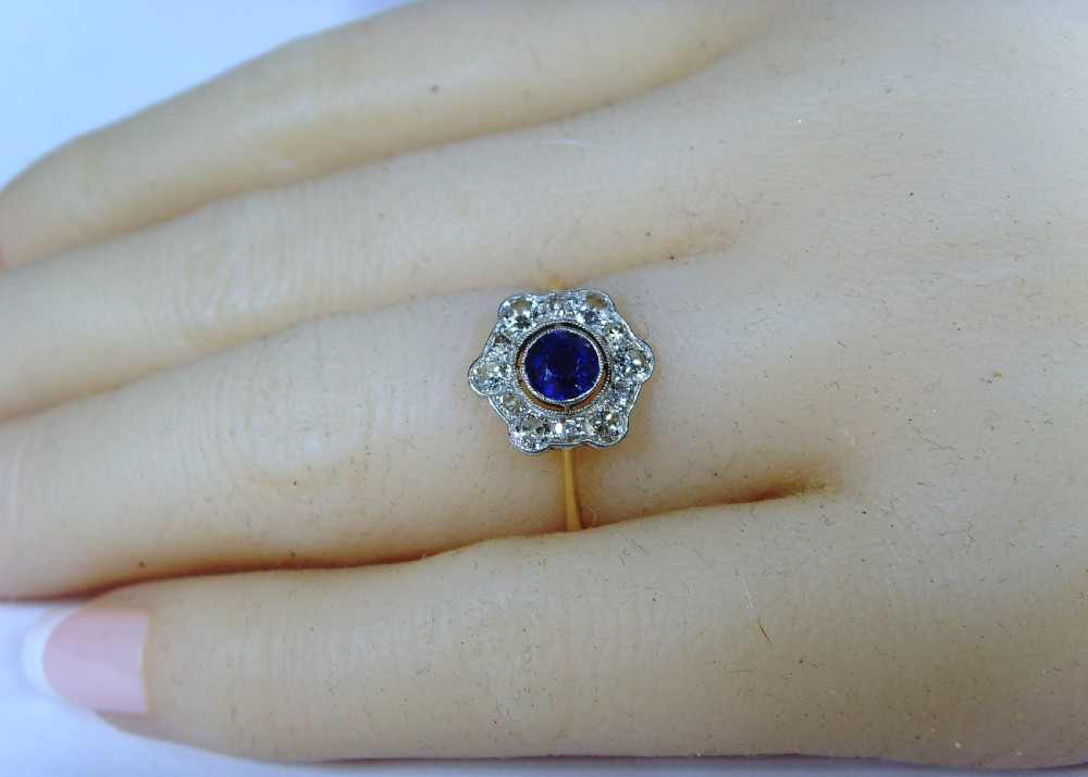 An Edwardian cluster ring featuring a central round blue sapphire surrounded by a halo of diamonds set in platinum with a yellow gold band. View V