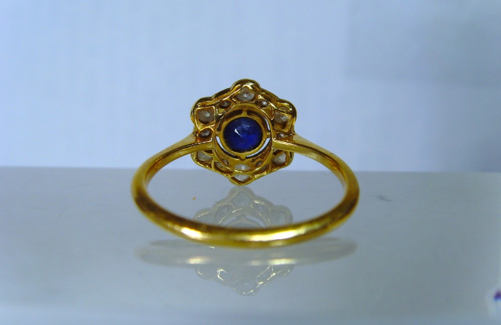 An Edwardian cluster ring featuring a central round blue sapphire surrounded by a halo of diamonds set in platinum with a yellow gold band. View VII