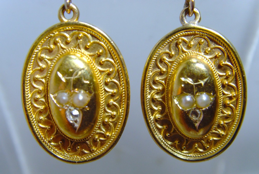 A pair of Victorian Etruscan Revival yellow gold oval drop earrings featuring central wirework detailing with seed pearls and diamonds suspended from chain links. View V