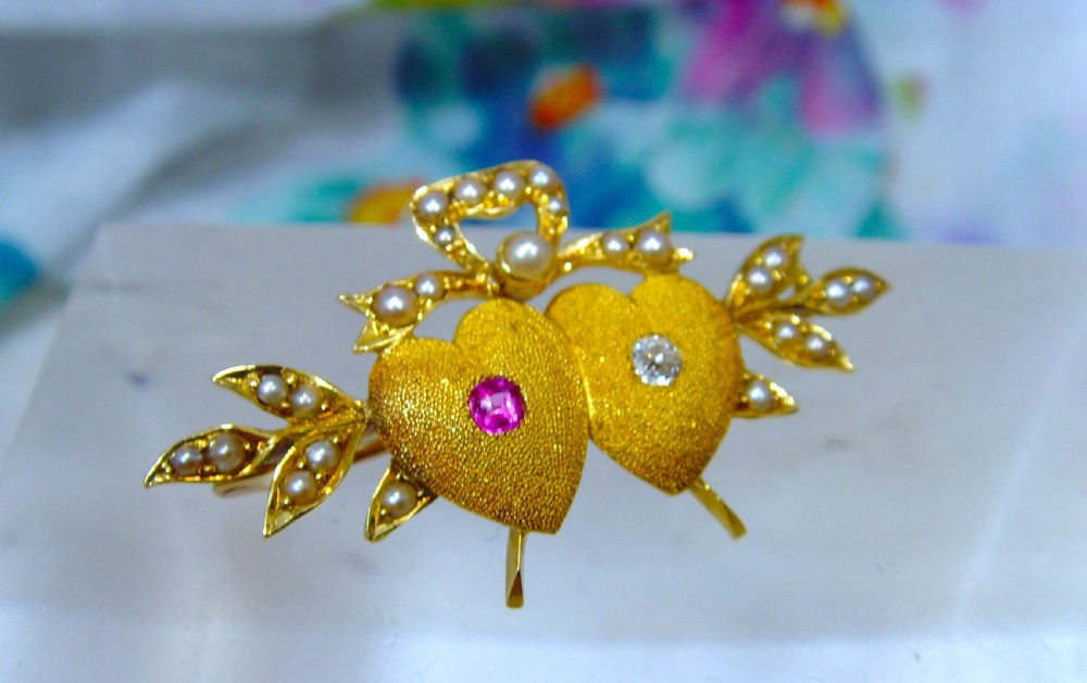 A Victorian 18ct yellow gold double heart brooch set with a ruby, a diamond, and seed pearl accents. View II