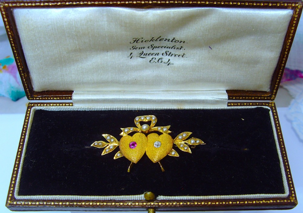 A Victorian 18ct yellow gold double heart brooch set with a ruby, a diamond, and seed pearl accents. View VII