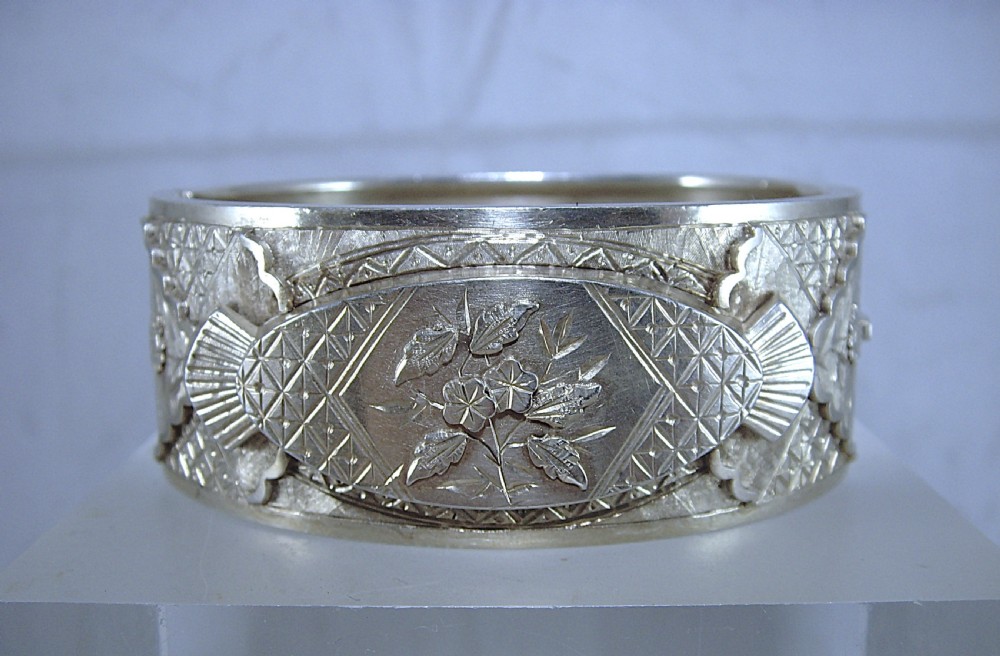 A wide Victorian sterling silver hinged cuff bangle featuring engraved floral motifs, geometric patterns, and fan details.