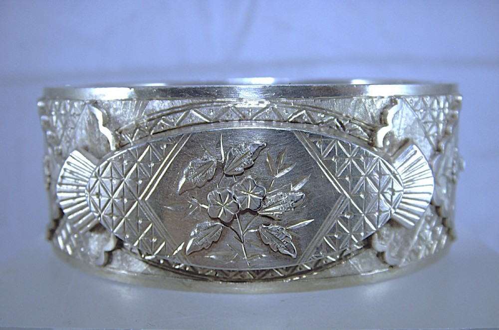 A wide Victorian sterling silver hinged cuff bangle featuring engraved floral motifs, geometric patterns, and fan details. View III
