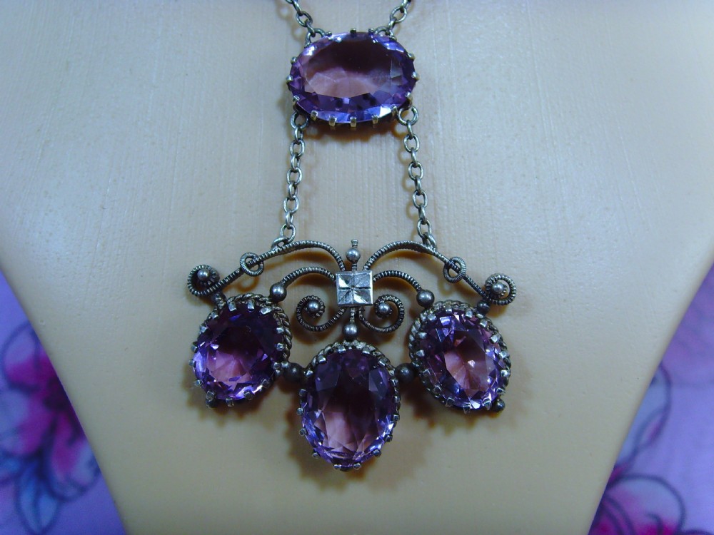 An Arts and Crafts era silver necklace featuring four faceted oval purple amethyst gemstones set within a scrollwork pendant suspended from a fine link chain. View II